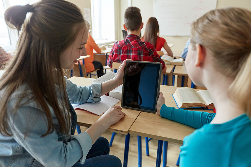 Two students in a classroom share a tablet